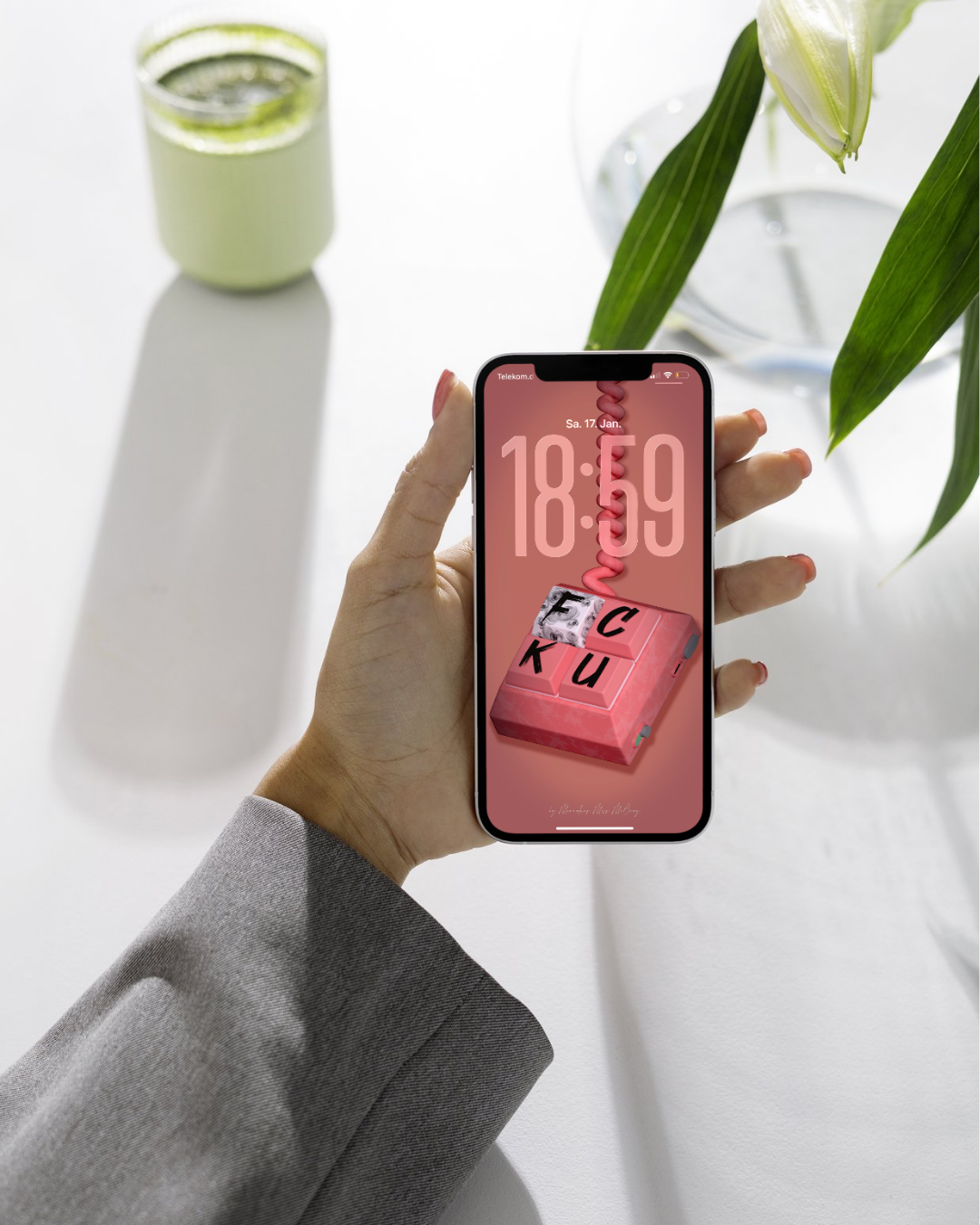 Das Bild zeigt ein iPhone mit einem individuellen Sperrbildschirm-Hintergrund. Der Hintergrund ist eine künstlerische Darstellung von zwei pinken Tasten einer Tastatur, auf denen die Buchstaben FC und KU abgebildet sind. Es handelt sich um eine digitale Illustration.